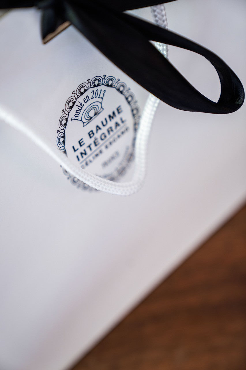Emballage cadeau blanc de la marque Le Baume Intégral de Céline Escand, logo doré et ruban noir, fondé en 2013
