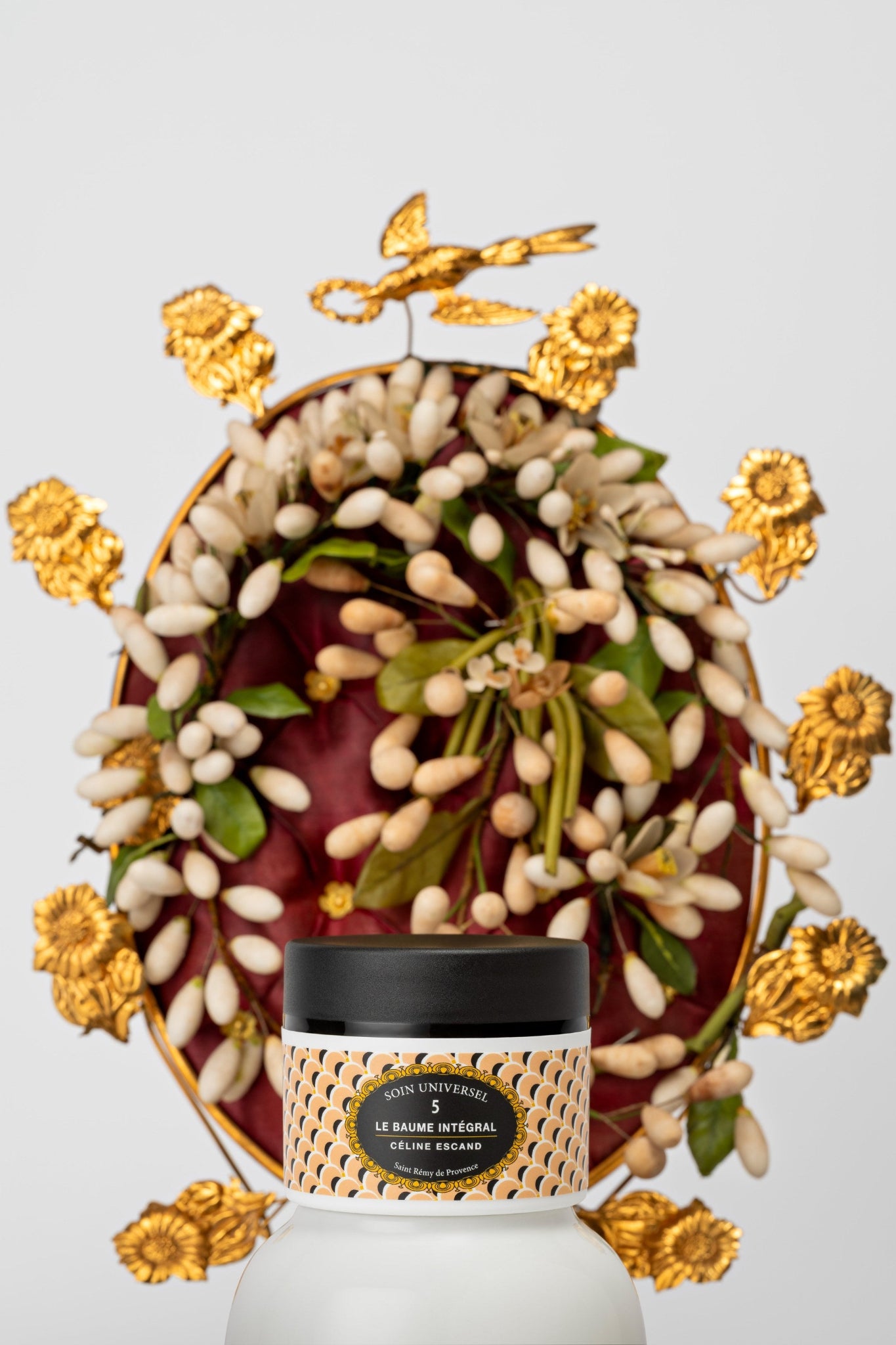 Pot du Baume Intégral n°5 à l'acide hyaluronique de Céline Escand, soin universel visage et corps, devant un cadre doré et des fleurs d'oranger de Provence
